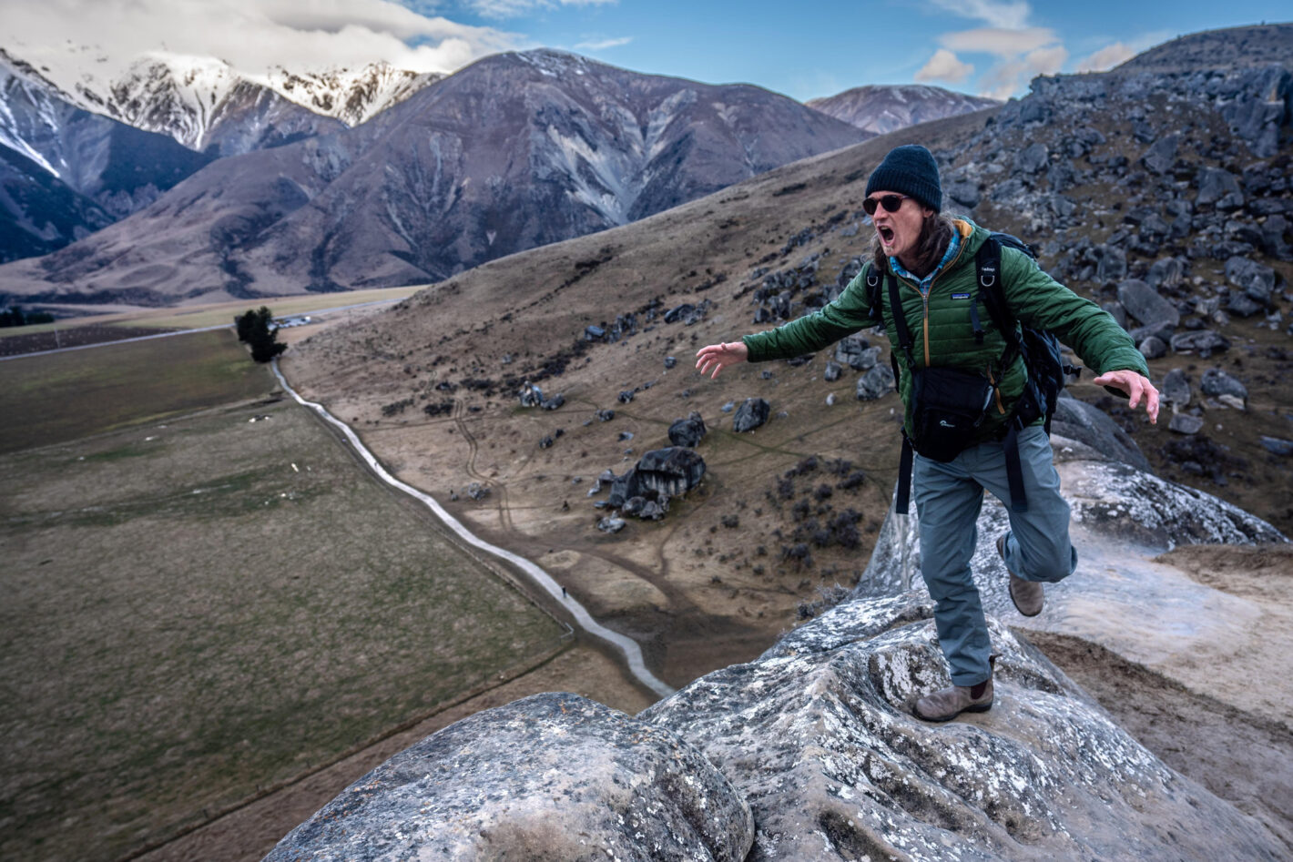 Jeremiah Watt stands fearlessly at the edge of an overhang, surrounded by a picturesque landscape.