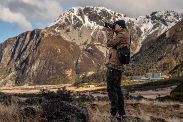 Watt captured taking a photo with his brown and tan clothing matching the mountain landscape behind him.