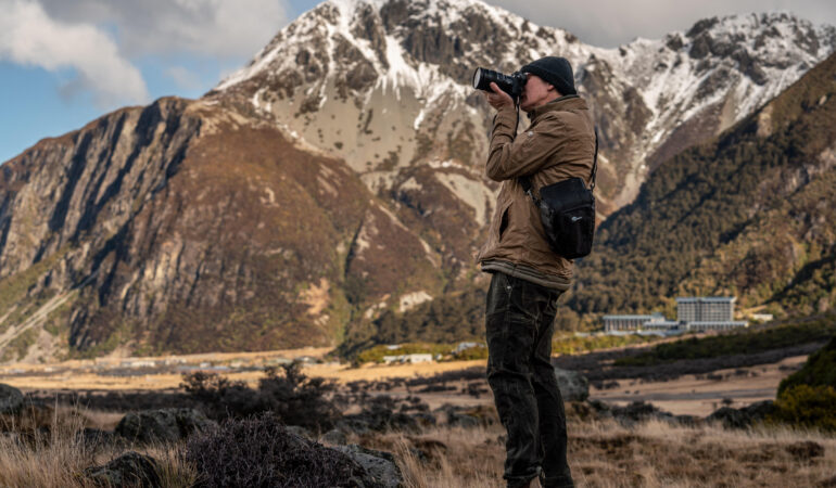 Watt captured taking a photo with his brown and tan clothing matching the mountain landscape behind him.