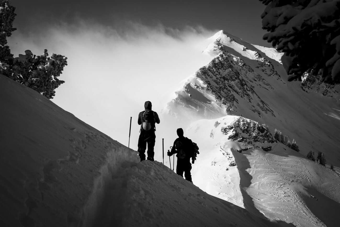 Backcountry skiers in black and white facing snow capped peaks