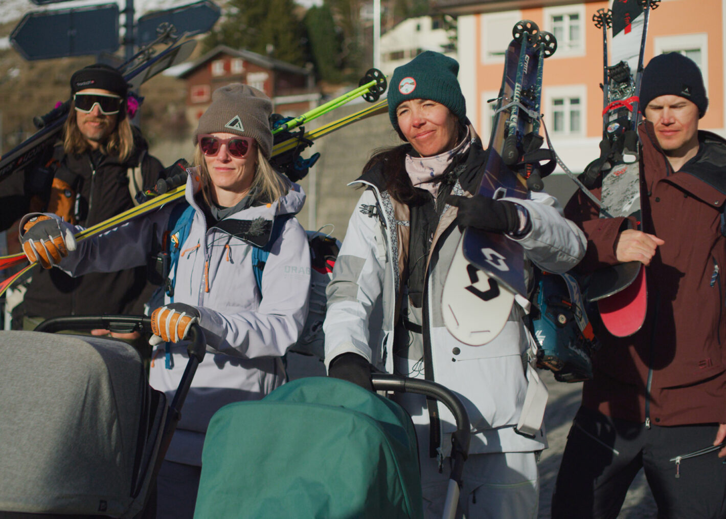 Elyse and three others walking in a parking lot with skis on their shoulders and gear on