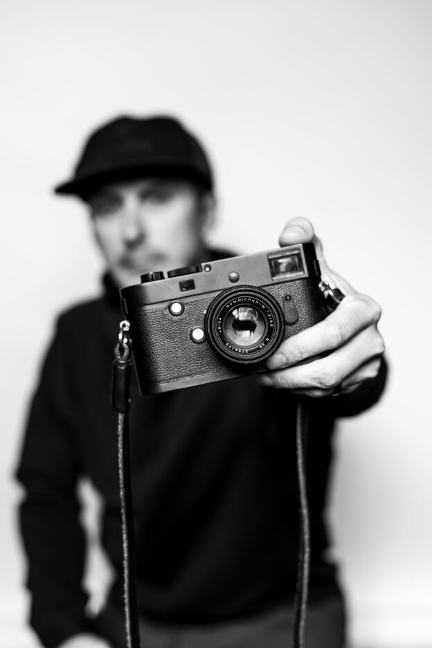 Blurred black and white background of man holding a camera, all focus centering on the camera in his hands