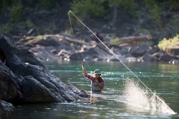 Image of Hilary fly fishing, waist-deep in a blue-green water.