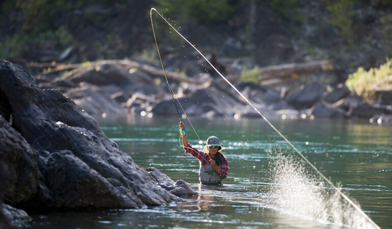 Image of Hilary fly fishing, waist-deep in a blue-green water.